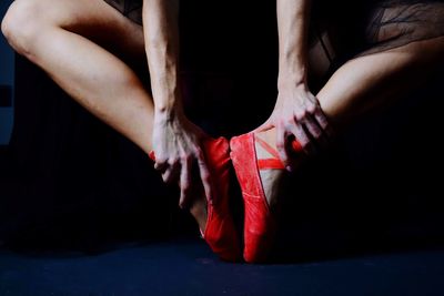 Low section of woman sitting on floor against black background