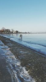 People walking on beach against clear sky during winter