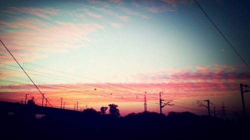 Low angle view of electricity pylon at sunset