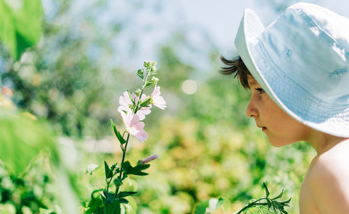 Child kid boy in panama hat breathing air, smelling flowers at garden on the grass, summer