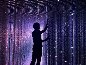 Rear view of silhouette man standing against illuminated light