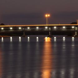 Illuminated bridge light reflecting on river at night