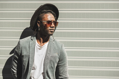 Young man wearing hat while standing against wall in city