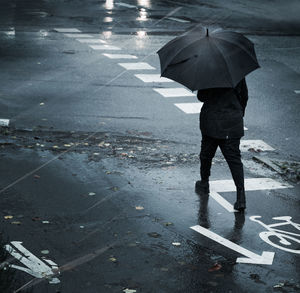 Man with umbrella walking on wet road during rainy season