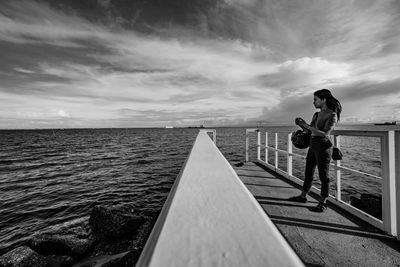 Side view of man standing on railing against sea