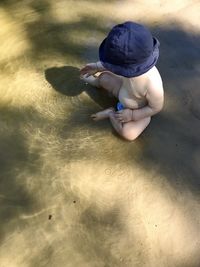 Baby boy in a blue panama hat sits on the shore of a pond and plays with water