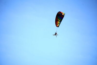 Low angle view of people paragliding against clear blue sky