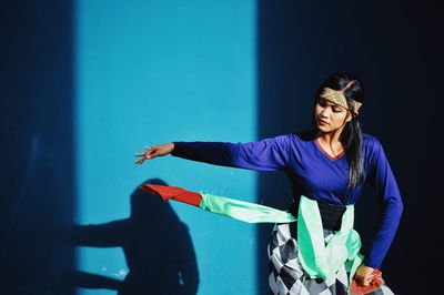 Young woman in traditional clothing dancing against wall