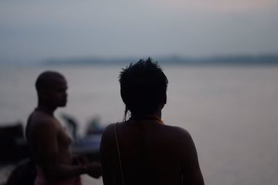 People standing at riverbank against sky during sunset