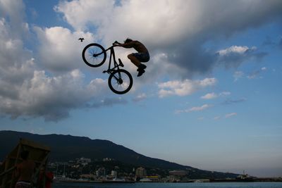 Man jumping bicycle against sky