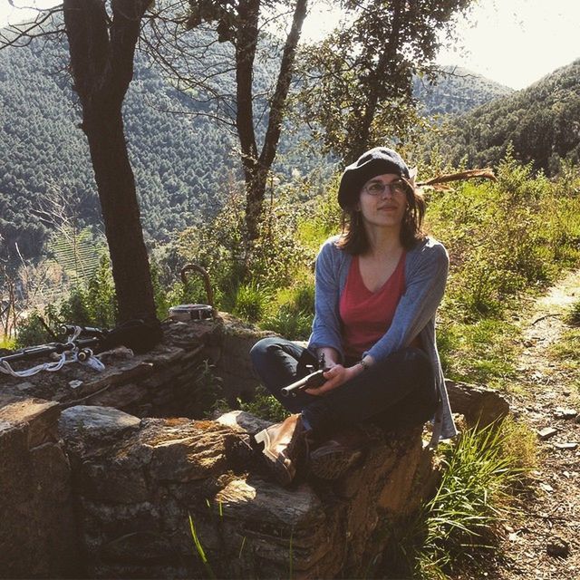 young adult, tree, casual clothing, lifestyles, person, leisure activity, looking at camera, portrait, forest, young women, standing, front view, sitting, nature, smiling, tree trunk, rock - object