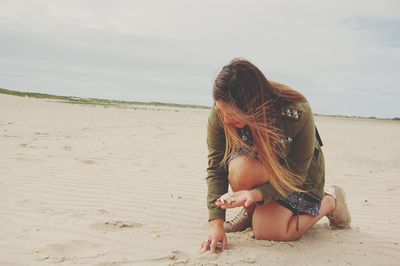 Young woman holding seashell at beach against sky