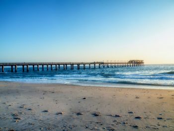 Pier on beach against clear blue sky