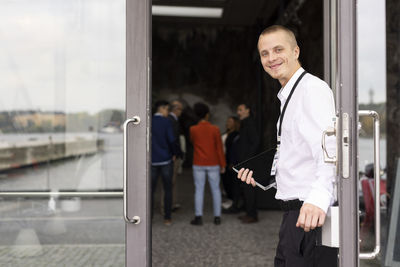 Portrait of smiling young businessman standing at doorway of convention center