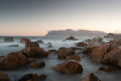 Rocks on sea shore against sky during sunset