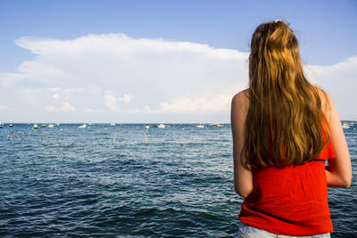 Rear view of woman standing by sea against sky