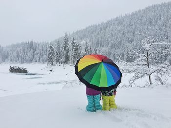 Rear view of people standing with colorful umbrella in blizzard