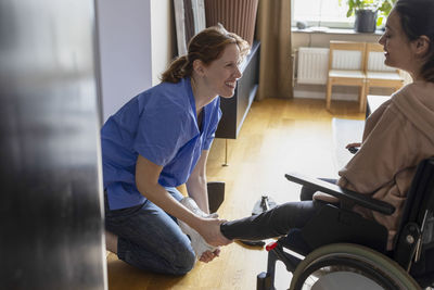 Happy nurse assisting woman with paraplegia while wearing shoes at home