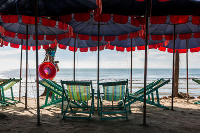 Red chairs on beach by sea against sky