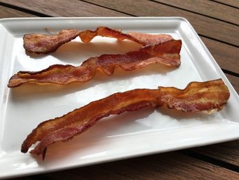 High angle view of bacon in white plate on wooden table