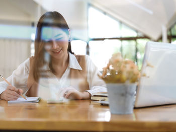 Young woman using phone while sitting on table