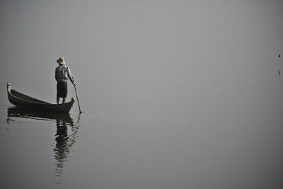 Rear view of fisherman standing on boat at lake