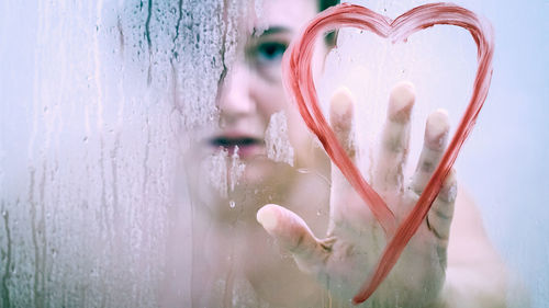 Woman touching heart shape on wet glass