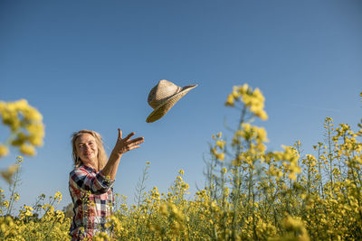 Portrait of a girl throwing a straw hat in a rapeseed field