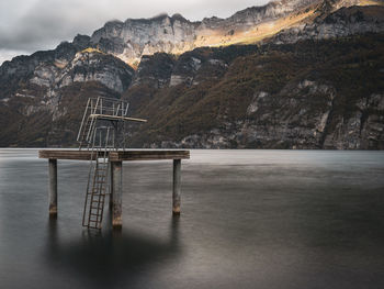 Scenic view of lake with abandoned diving tower and mountains against sky