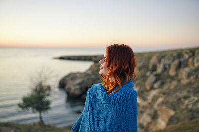 Woman standing by sea against sky during sunset