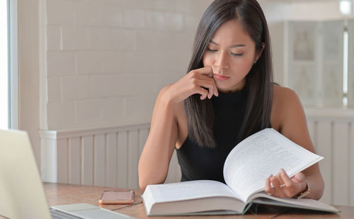 Young woman reading book while sitting on table