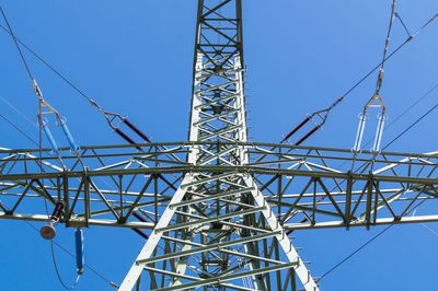 Low angle view of electricity pylon against blue sky