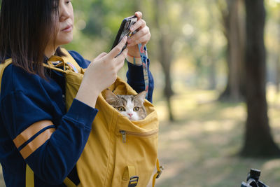 Asian woman use phone and biking bicycle with her cat in backpack at park