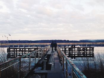Rear view of people walking on pier over river