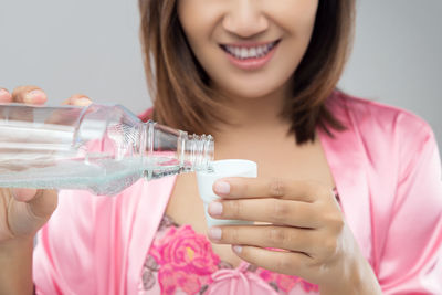 Midsection of smiling woman pouring mouthwash from bottle in lid against gray background