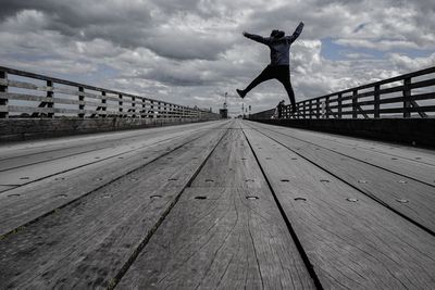 Low angle view of man jumping on footbridge