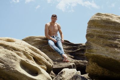 Young man standing on rock against sky