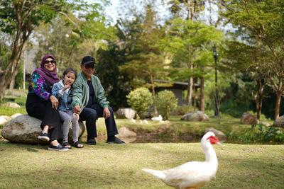 Full length of group of people sitting on the rock looking duck pass away