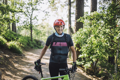 Portrait of man wearing protective clothing standing with cycle on footpath