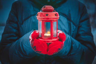 Man holding a red candle lantern with a candle close up. a man dressed in a warm coat and red gloves