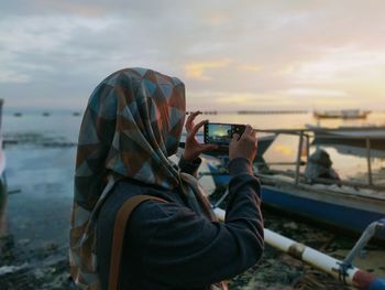 Woman photographing with camera against sky during sunset