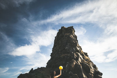 Low angle view of woman holding ball by rock formation against sky