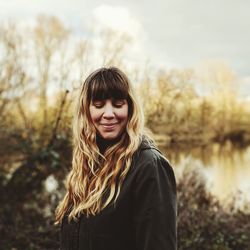 Smiling woman with blond hair standing against trees in forest