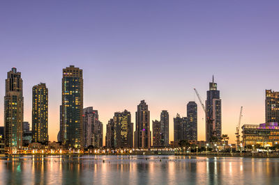 Illuminated buildings by city against sky at dusk