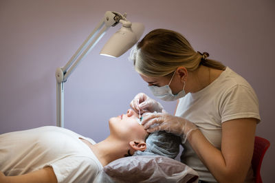 Beautician wearing mask treating woman in spa