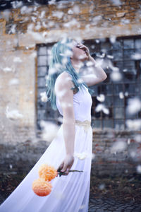 Beautiful woman with flower standing against wall during snowfall