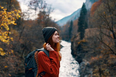 Young woman looking away while standing against trees