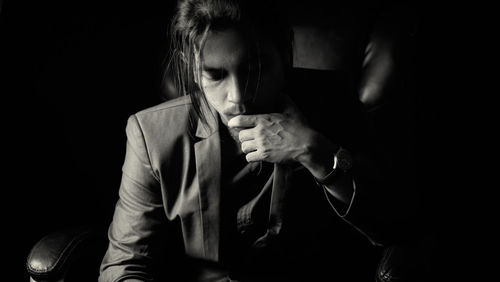 A long haired young business man wearing a suit thinking on revolving chair in darkness.
