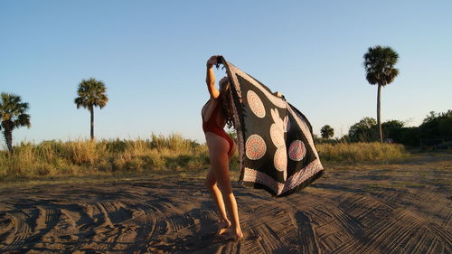 Full length of young woman wearing one piece swimsuit holding scarf on sand