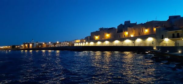 Illuminated buildings by river against sky at night